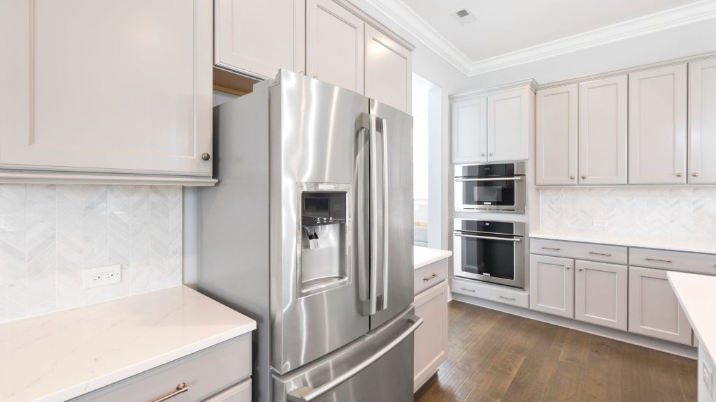 Modern kitchen with light gray cabinets, stainless steel French door refrigerator, built-in double ovens, white countertops, and herringbone tile backsplash. Appliance technicians in Middlesex County can handle same day appliance repair for this bright space.