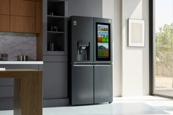 A modern black double-door refrigerator with a built-in touchscreen display stands in a bright, contemporary kitchen, perfectly maintained by MA appliance services for reliable repairs for appliances.