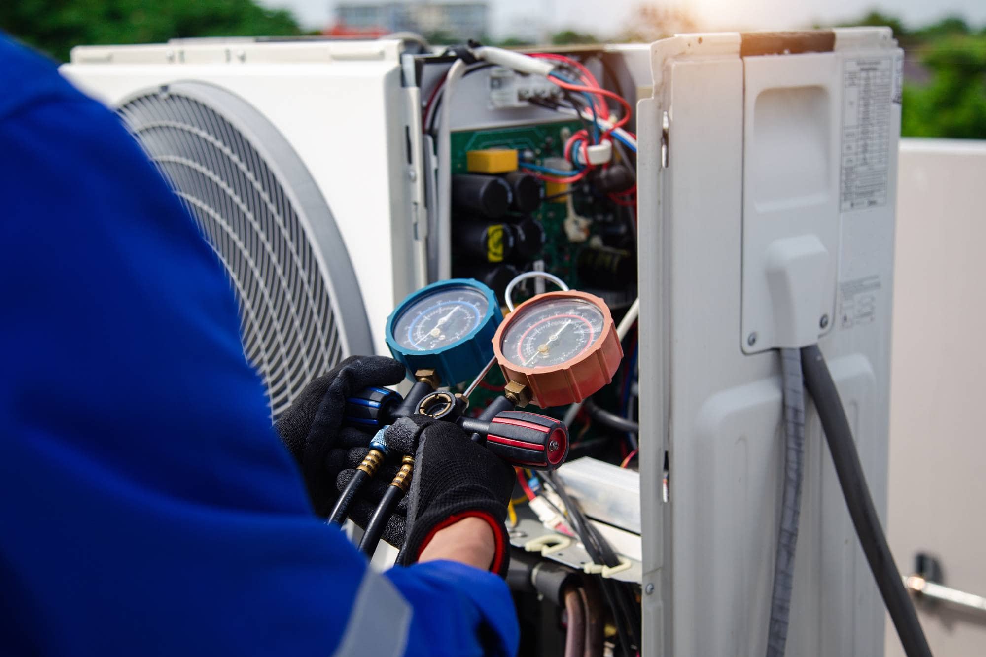 A technician in blue overalls checks an air conditioning unit using pressure gauges and tools, with the system’s internal wiring and components exposed—demonstrating expert Middlesex County, MA appliance services.