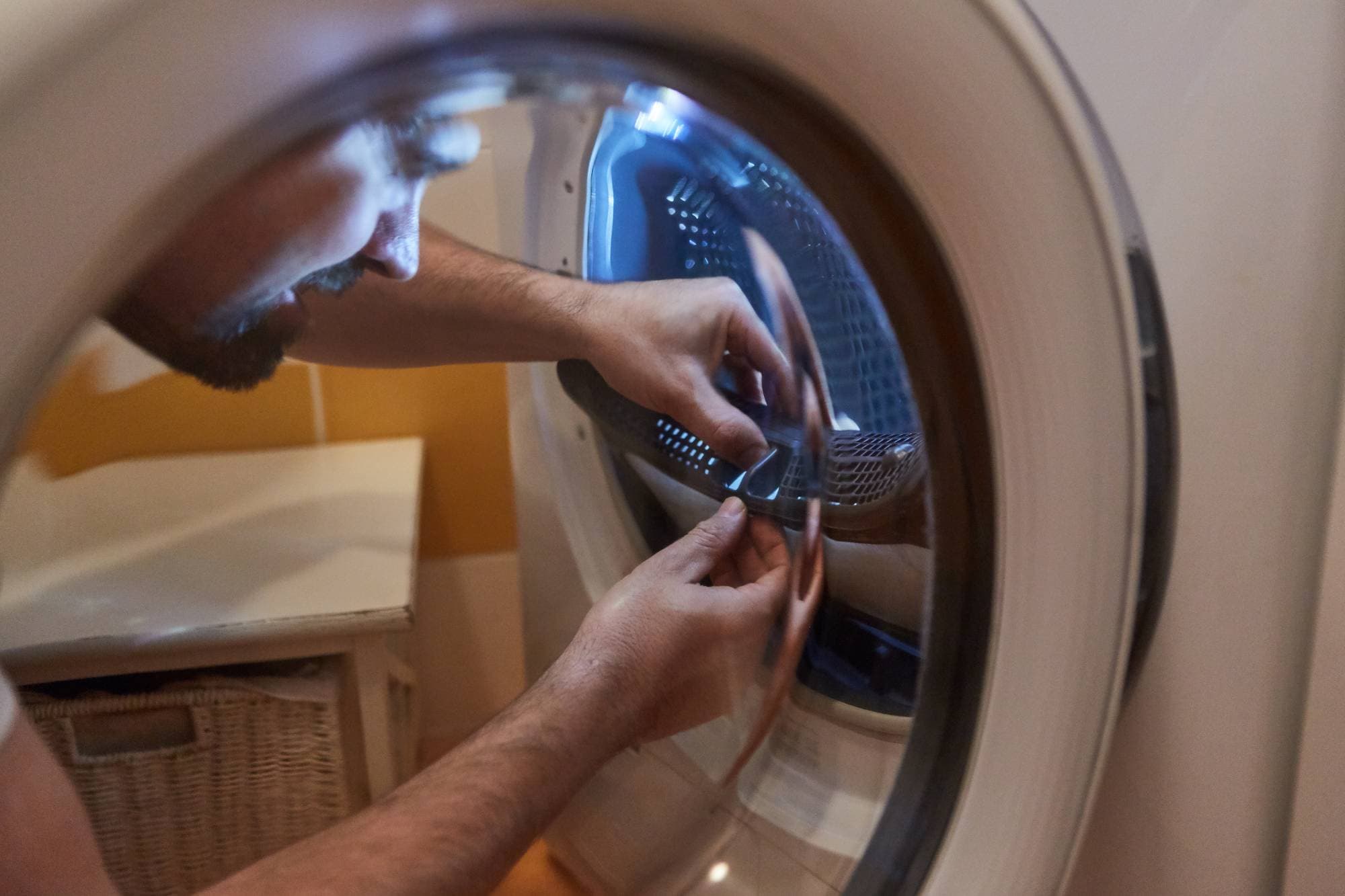 An appliance technician in Middlesex County is repairing or inspecting the inside of a front-loading washing machine, reaching into the drum with both hands, as seen through the open door during repairs for appliances.