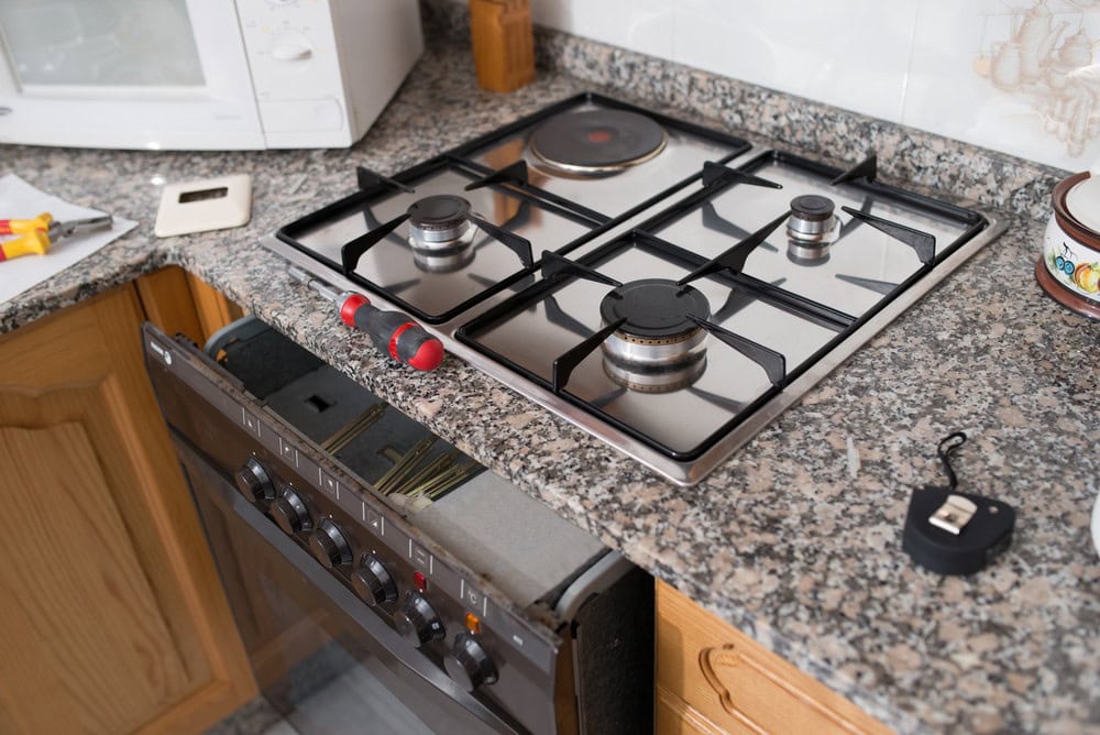 A gas stove with four burners is set in a granite countertop. A screwdriver, tape measure, and some tools are nearby, suggesting MA appliance services or appliance technicians in Middlesex County are handling installation or maintenance work.